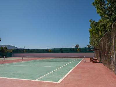Leerer Tennisplatz mit Zaun und Bäumen unter klarem Himmel