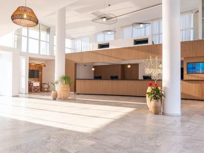 Bright hotel lobby with marble floor, wooden reception desk and large windows.