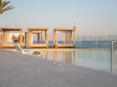 Poolbereich mit drei weißen Tagesbetten und Palmen bei Sonnenuntergang