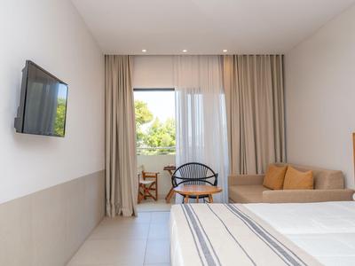 Helles Hotelzimmer mit zwei Betten, Sofa, Stuhl und Blick nach draußen.