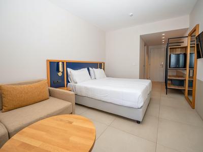 Helles Hotelzimmer mit großem Bett, Sofa, Holzspieltisch und moderner Einrichtung.