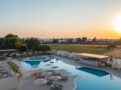Großer Poolbereich mit Liegestühlen und Sonnenschirmen bei Sonnenuntergang, umgeben von Feldern.