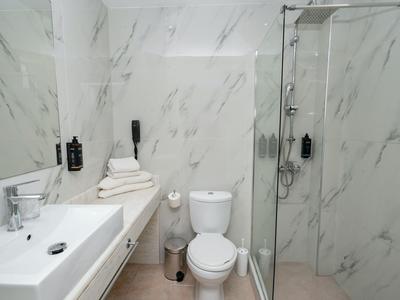 Modernes Hotelduschbad mit Glasabtrennung, Toilette und Waschbecken auf Marmorfliesen.