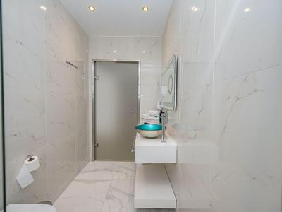 Modernes Badezimmer mit weißem Marmor, Glaswaschbecken und hellen Wänden.