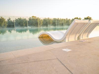 Moderne weiße Liegestühle am Rand eines ruhigen Pools mit Glasgeländer.