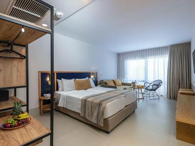 Modernes Hotelzimmer mit Doppelbett, Sitzbereich, Fernseher und großem Fenster mit Vorhängen.