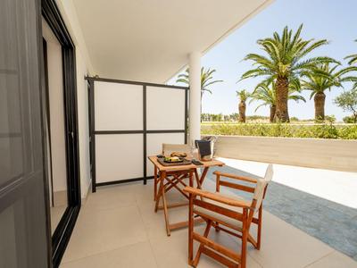 Balkon mit zwei Holztischen und Stühlen mit Blick auf Palmen und Garten.