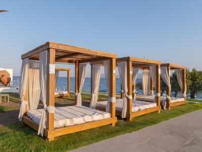 Strandbetten mit weißem Vorhang auf grünem Rasen bei sonnigem Himmel, nahe Wasser.