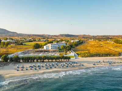 Hotelanlage am Strand mit Sonnenschirmen und Blick auf Hügel bei klarem Himmel.