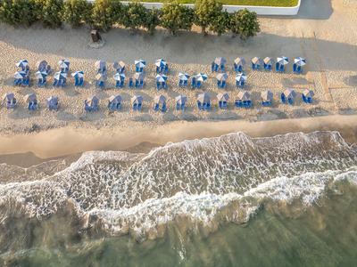 Luftaufnahme eines Strandes mit Sonnenliegen und Schirmen entlang der Küste.