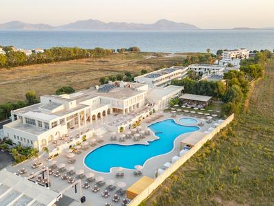 Modernes Hotel mit großem Pool, umgeben von Feldern und Meer im Hintergrund.
