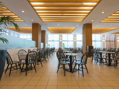 Heller, moderner Hotel-Speisesaal mit Holzbalkendecke, Pflanzen und schwarzen Stühlen.