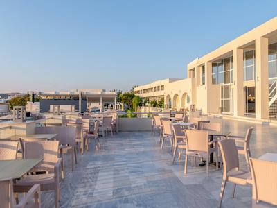 Außenbereich eines modernen Hotels mit Tischen und Stühlen auf einer Steinveranda bei Sonnenuntergang.