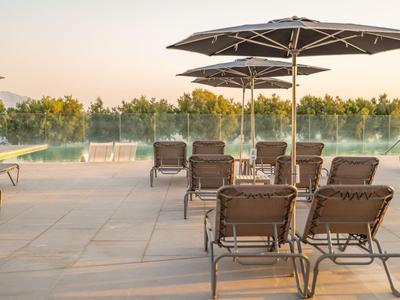 Leerer Poolbereich mit Liegestühlen und Schirmen, umgeben von Bäumen im Sonnenuntergang.
