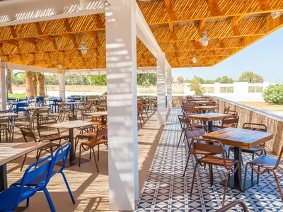 Offener Hotelrestaurantbereich mit Holzdach, bunten Stühlen und gemustertem Boden unter natürlichem Licht.