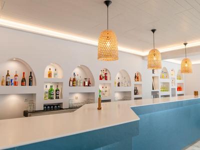 Moderner Hotelbarschalter mit blauem Tresen und hängenden Flechtlampen bei weißer Wand.