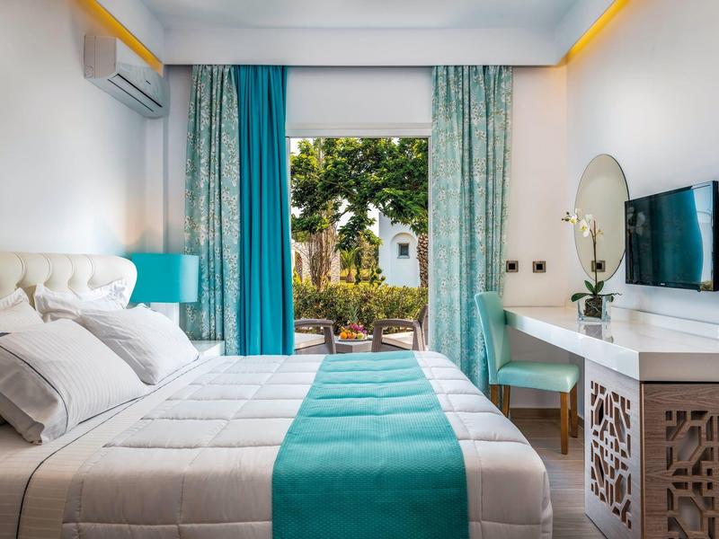 Bright hotel room with double bed, turquoise curtains, and garden view.