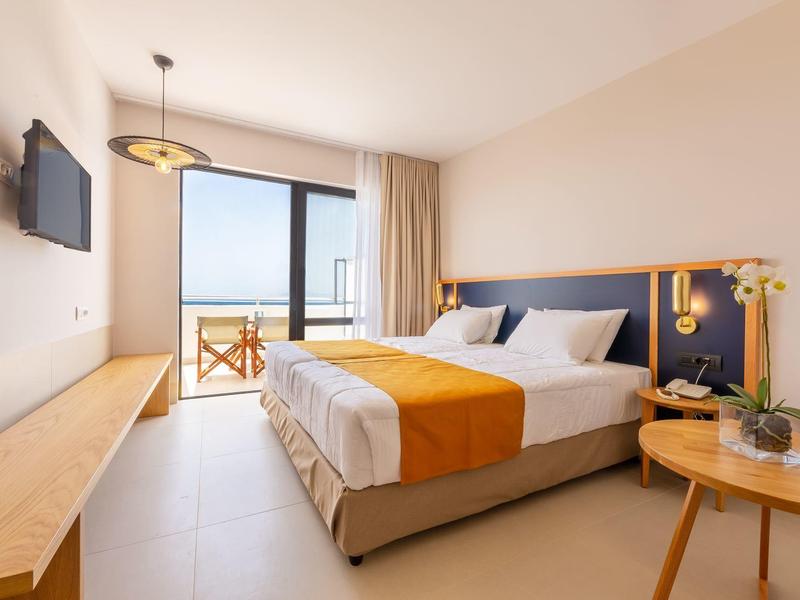 Modern hotel room with double bed, TV, balcony, and sea view.