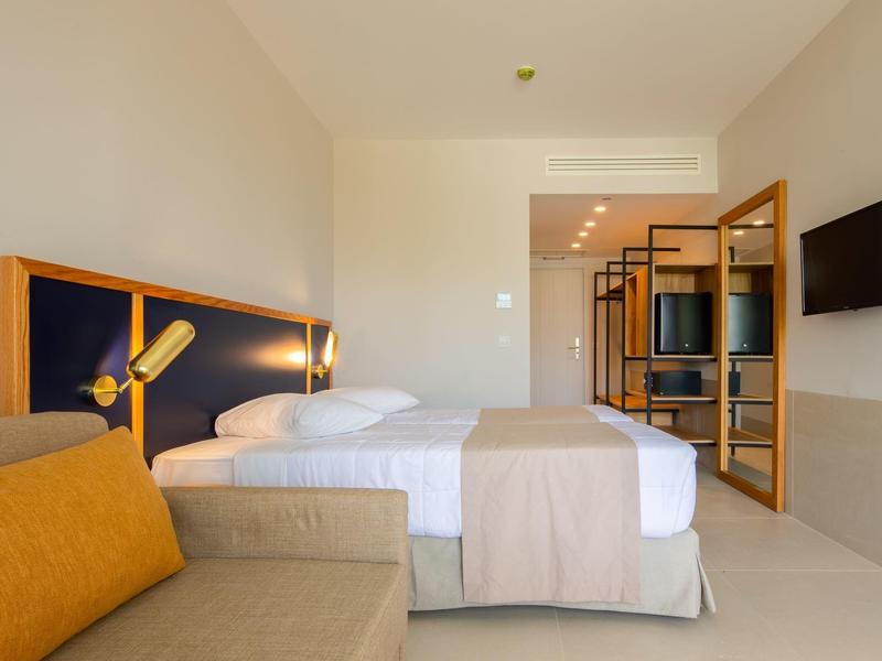 Modern hotel room with double bed, sofa, and flat-screen TV.