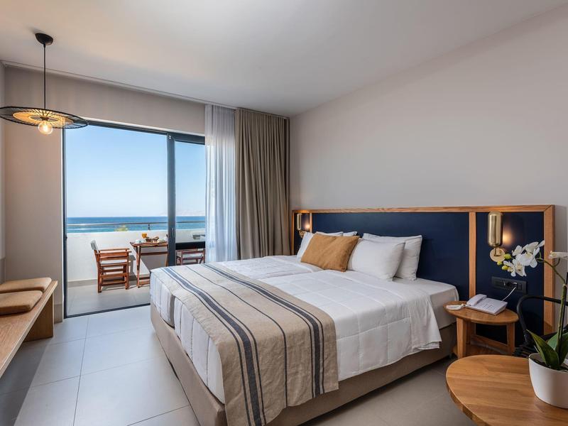 Modern hotel room with double bed, balcony, and sea view.