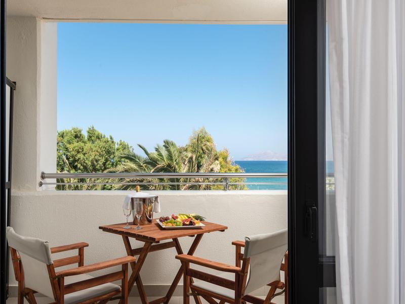 Balcony with table and chairs, view of the sea and palm trees under clear sky.