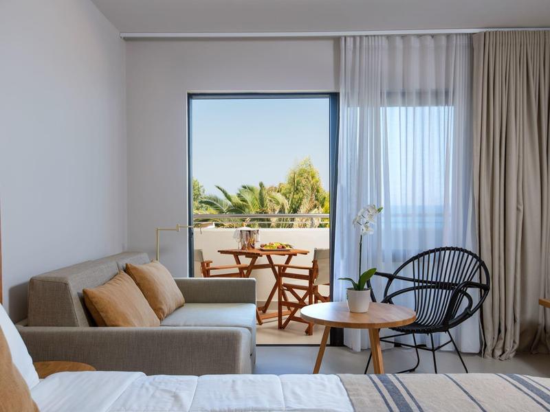 Modern hotel room with balcony, seating area, and greenery view.