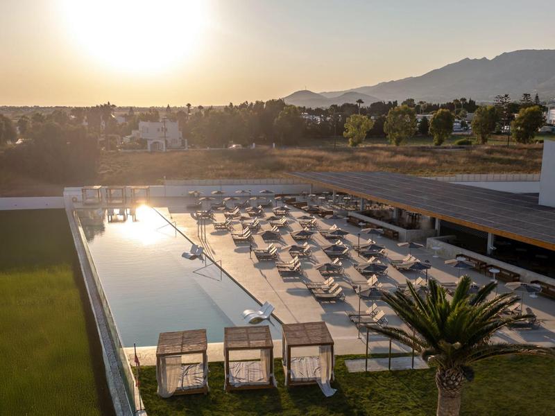 Modern hotel pool area at sunset with lounge chairs and palm trees.