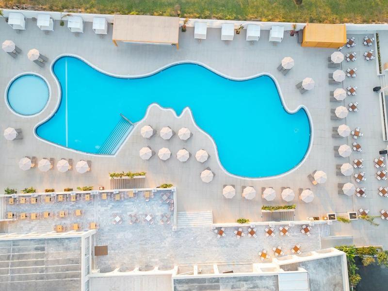 Large irregular-shaped pool with many loungers and umbrellas in a hotel area.