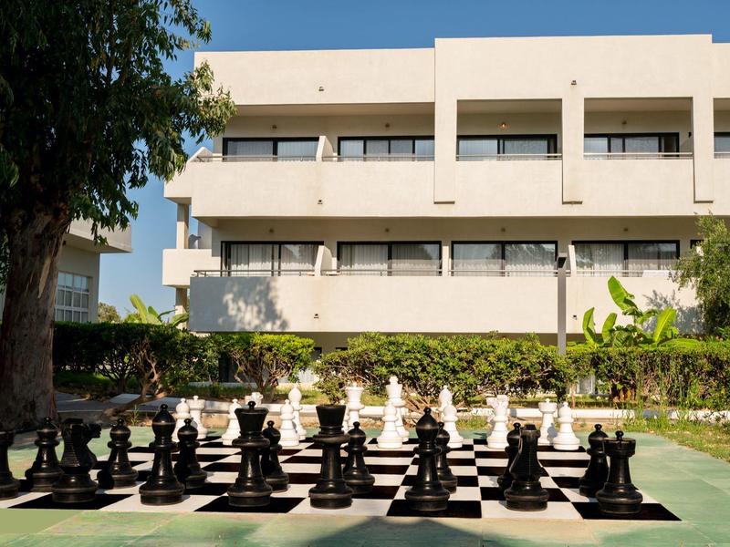 Large outdoor chess set in front of a multi-story building under clear sky.