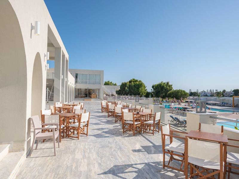 Terrace with wooden tables and chairs beside pool under clear blue sky.