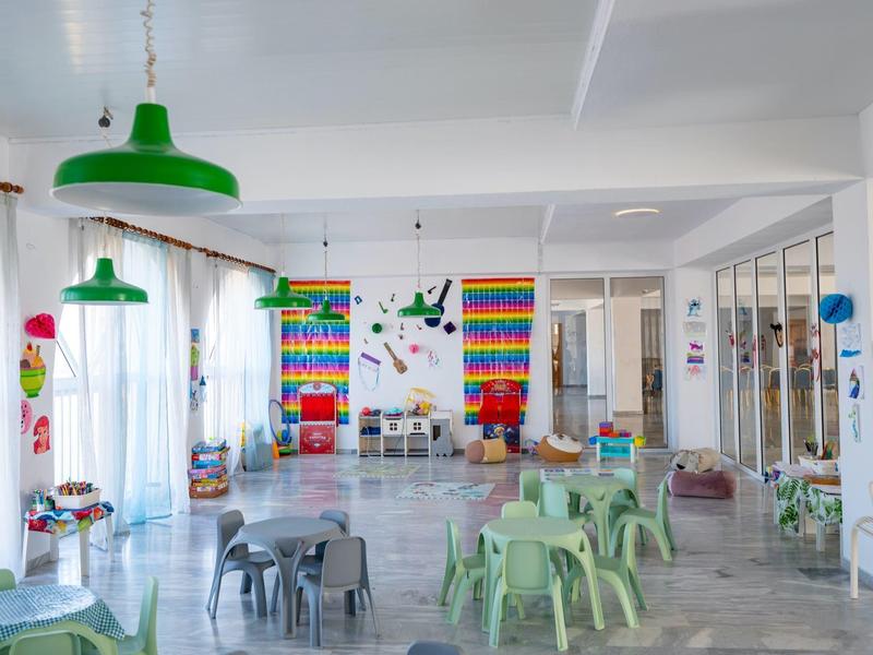 Bright, cheerful room with children's tables, chairs, colorful shelves, and green lamps.