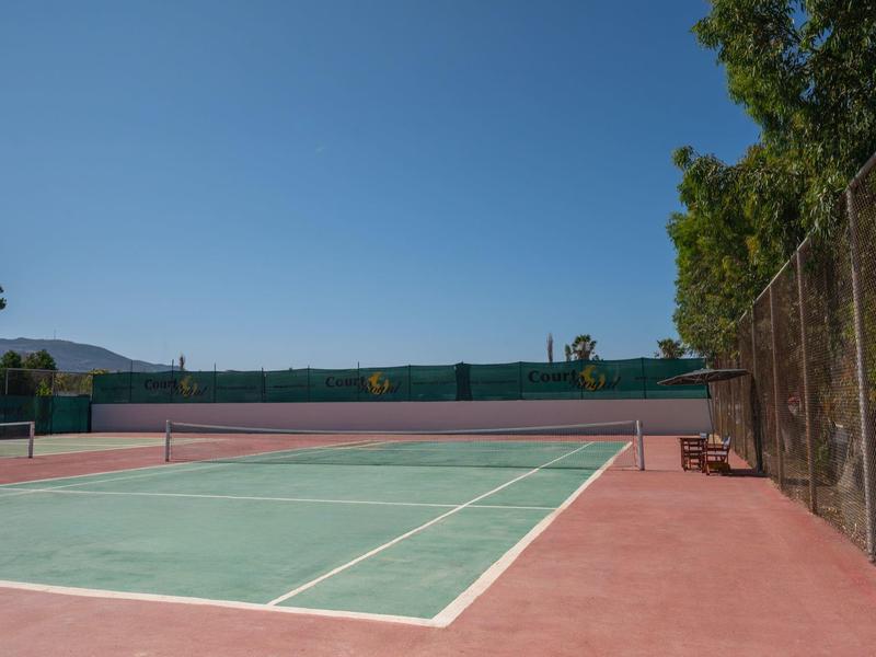 Empty outdoor tennis court with blue sky and green landscape in the background.