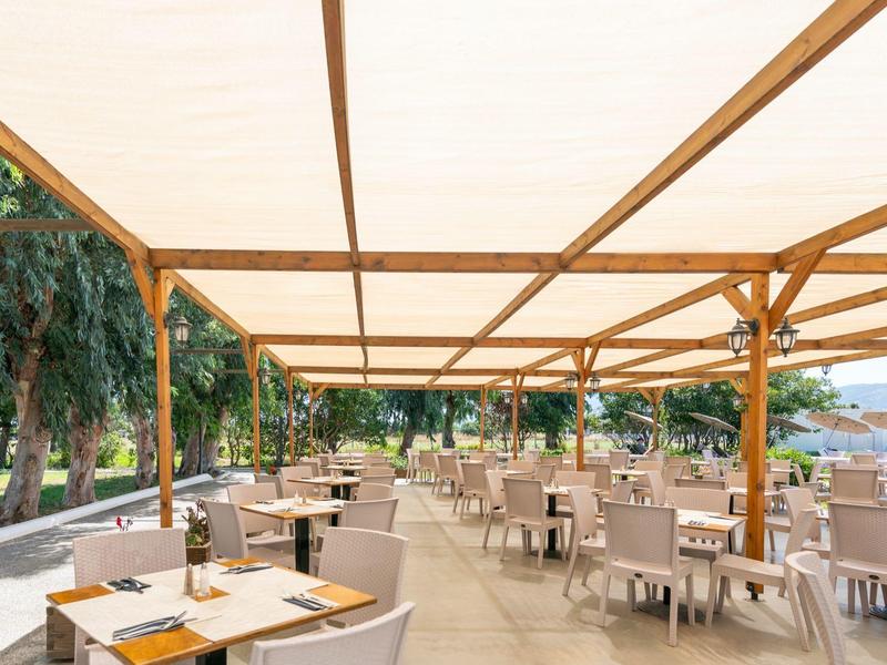 Spacious covered outdoor terrace with wooden furniture and white cushions at a hotel.