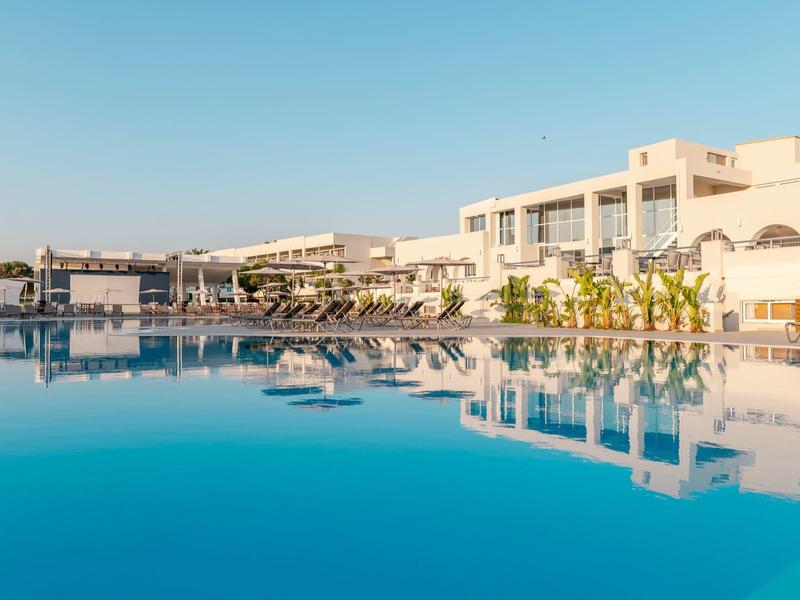 A calm pool in front of a white hotel building under clear sky.