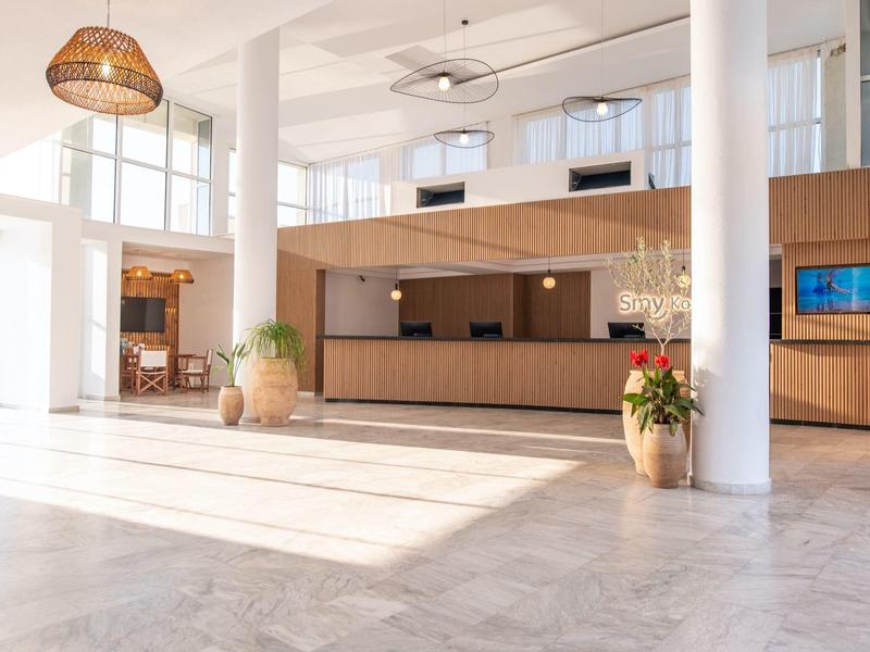 Bright hotel lobby with marble floor, wooden reception desk and large windows.
