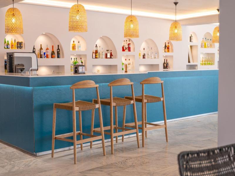 Modern hotel bar area with a blue counter, three wooden stools, and warm pendant lights.