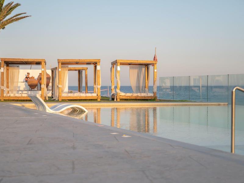 Luxury pool area with loungers and cabanas, sea view at sunset.