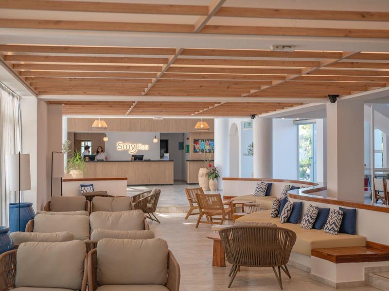 Bright, modern hotel lounge with comfortable armchairs, wooden beam ceiling, and large windows.