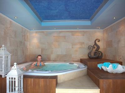 Persona relajada en jacuzzi en sala elegante tipo spa con escultura de bronce.