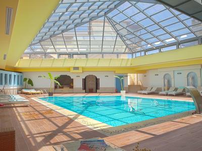 Gran piscina cubierta con techo de cristal y tumbonas en un hotel.