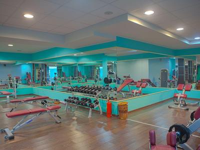Moderne fitnessruimte met gewichten, trainingsbanken en spiegels in een hotel.