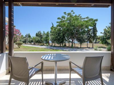 Vista desde una terraza cubierta con dos sillas y mesa hacia árboles verdes y cielo azul.