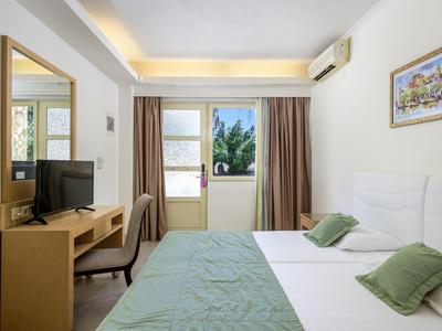 Habitación de hotel luminosa con cama doble, escritorio, televisor y ventana con vista a árboles.