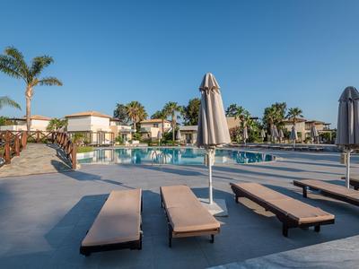 Leeg zwembadgebied met ligbedden en parasols voor hotelgebouwen onder heldere lucht.