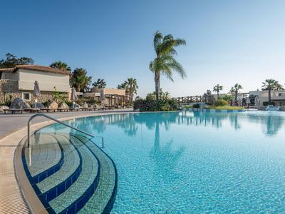 Groot buitenzwembad met trappen en palmbomen bij een hotel onder een heldere hemel.