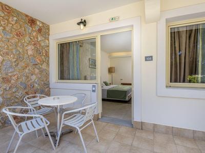 Terraza con mesa de jardín blanca y tres sillas junto a una habitación con puerta y ventana abiertas en un hotel.