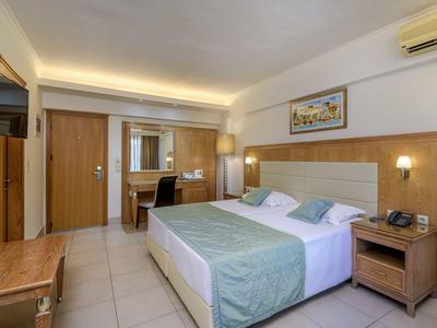 Habitación de hotel luminosa con cama grande, escritorio, TV e iluminación elegante.