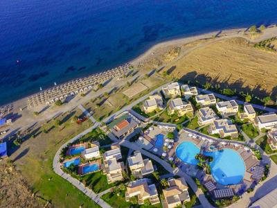 Vista aérea de un resort en la playa con piscinas y sombrillas junto al mar.