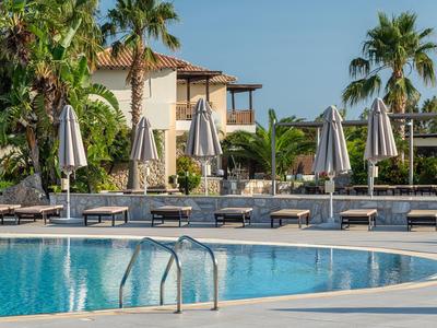 Hotelpool mit Liegestühlen, Sonnenschirmen und mediterranen Gebäuden im Hintergrund.