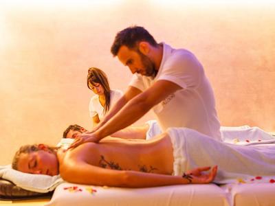 Ein Mann erhält eine Massage auf einer Liege draußen mit zwei weiteren Personen im Hintergrund.